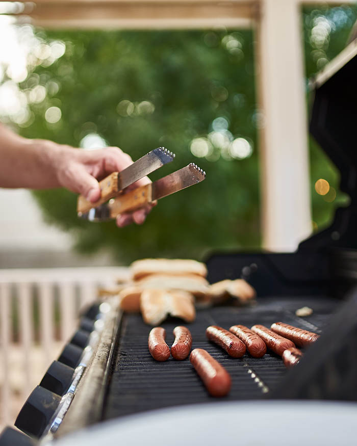 man grilling hot dogs on propane powered grill